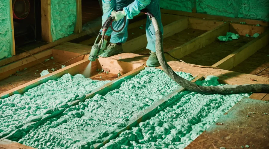 Male builder insulating wooden frame house. Cropped view of man worker spraying polyurethane foam on floor inside of future cottage, using plural component gun. Construction and insulation concept.